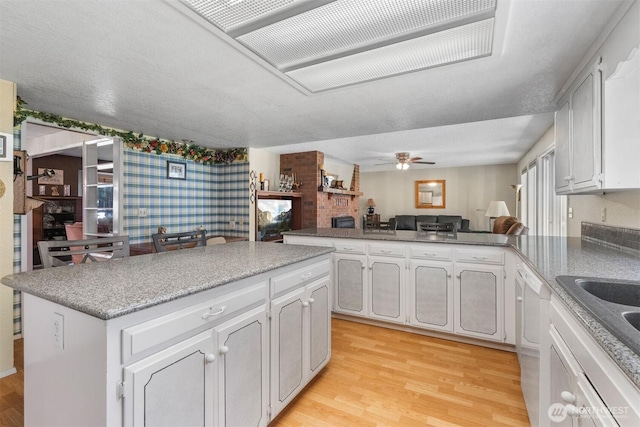 kitchen with a ceiling fan, white cabinets, a peninsula, open floor plan, and light wood-style flooring