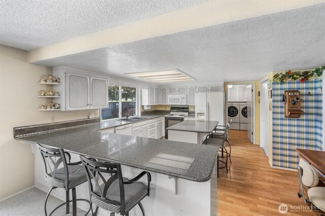 kitchen featuring a breakfast bar, a sink, white appliances, a peninsula, and washer and clothes dryer
