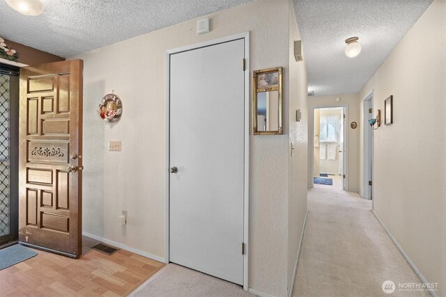 corridor with baseboards, a textured ceiling, wood finished floors, and visible vents