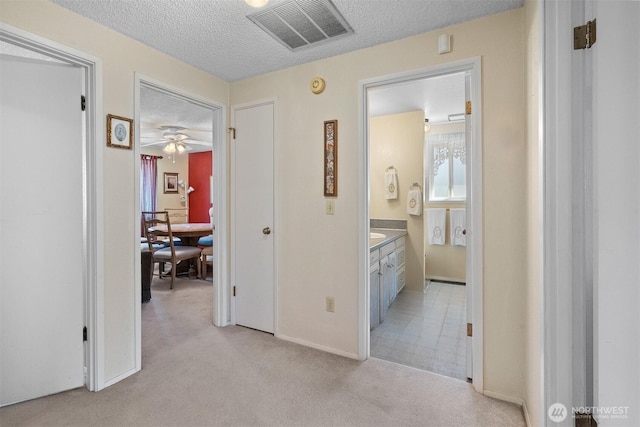 hallway with baseboards, light colored carpet, a textured ceiling, and visible vents