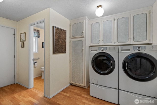 washroom featuring cabinet space, a textured ceiling, washing machine and dryer, and light wood-style floors