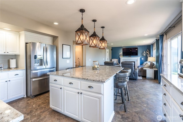 kitchen with a kitchen bar, stainless steel refrigerator with ice dispenser, stone finish flooring, a center island, and a fireplace