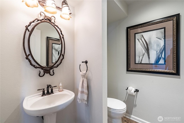 bathroom featuring toilet, baseboards, and a sink