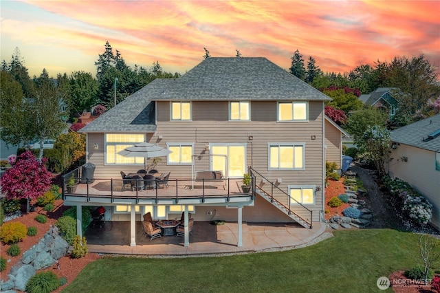 back of house at dusk with a yard, roof with shingles, a patio area, and a deck