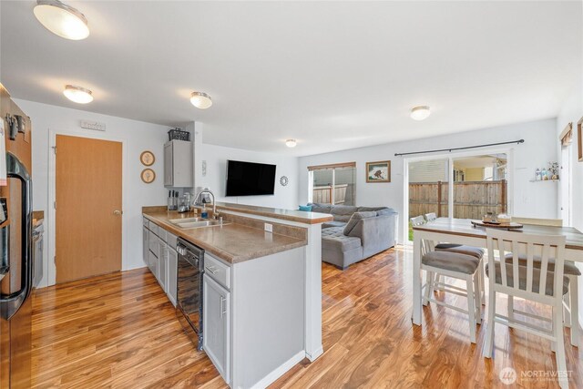 kitchen with a sink, light wood finished floors, a peninsula, and open floor plan