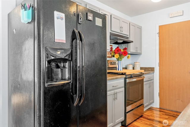 kitchen with stainless steel electric range, black refrigerator with ice dispenser, under cabinet range hood, and light wood finished floors