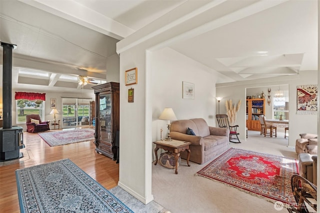 living room featuring a ceiling fan, beam ceiling, a wood stove, and wood finished floors