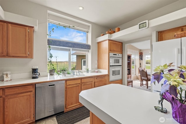 kitchen with brown cabinetry, white appliances, recessed lighting, light countertops, and a sink