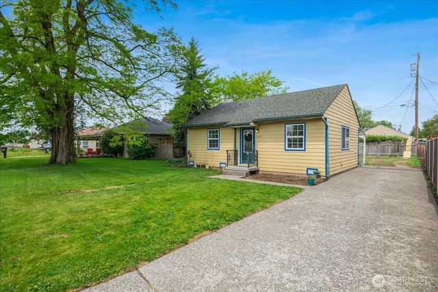 view of front facade with a shingled roof, aphalt driveway, fence, and a front yard