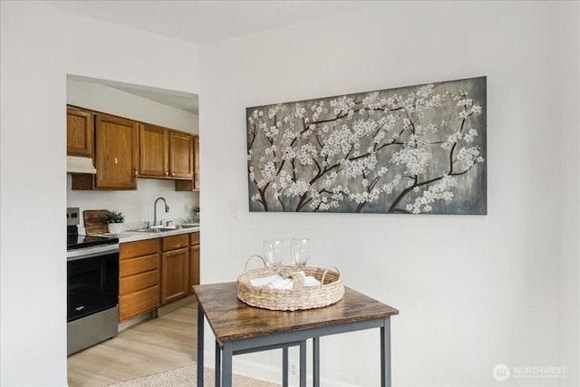 kitchen featuring stainless steel electric range, a sink, light countertops, brown cabinetry, and under cabinet range hood