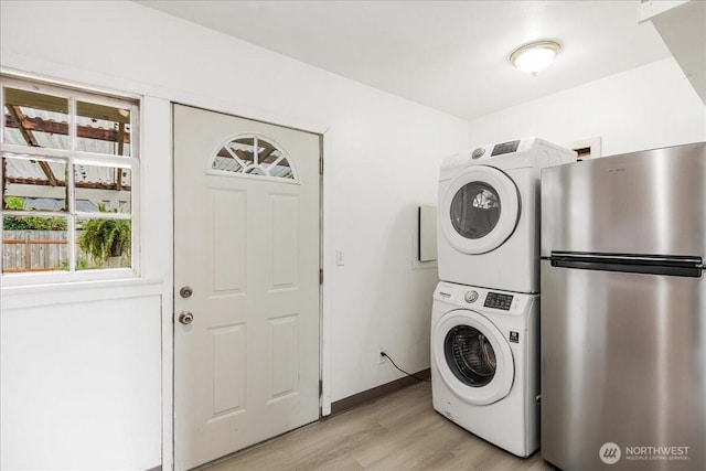 clothes washing area featuring stacked washing maching and dryer, light wood-style floors, laundry area, and a healthy amount of sunlight