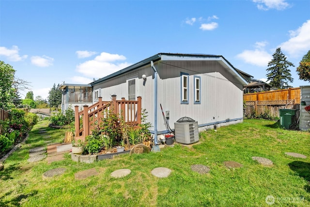 view of side of home with central AC, fence, a yard, and a sunroom