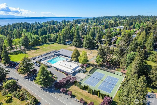 drone / aerial view of a pool area, a nearby body of water, and a forest