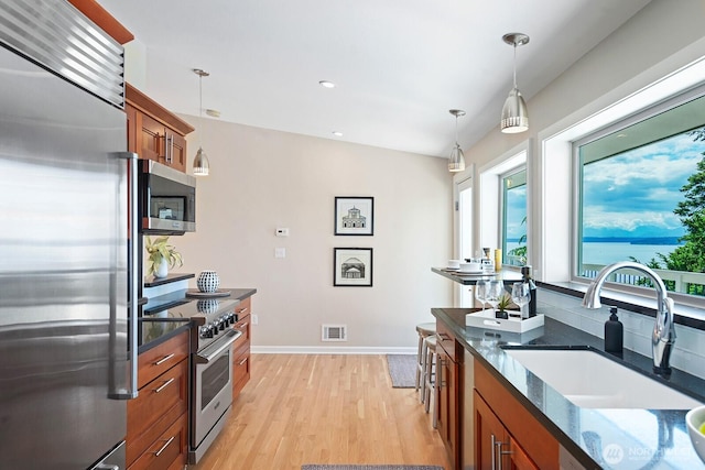 kitchen with premium appliances, a sink, brown cabinetry, healthy amount of natural light, and recessed lighting