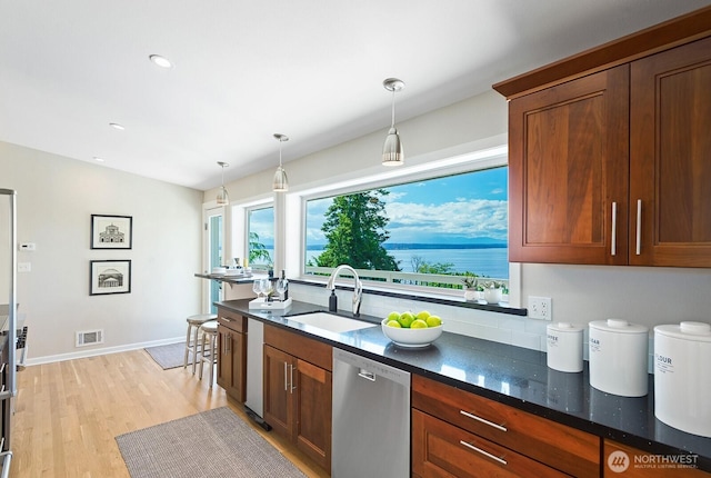 kitchen with dishwasher, a sink, decorative light fixtures, dark stone countertops, and light wood-type flooring