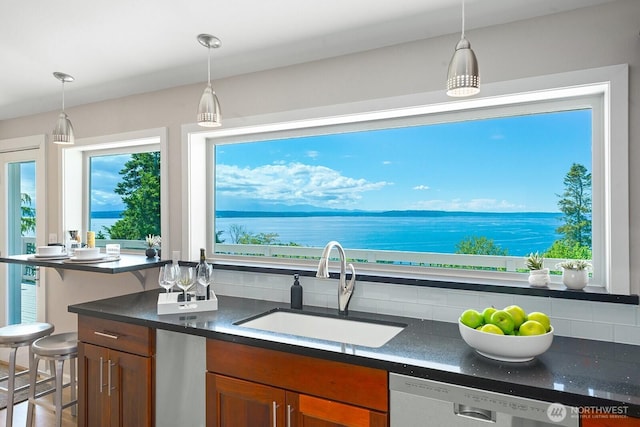 kitchen with a sink, dark countertops, dishwashing machine, pendant lighting, and brown cabinets