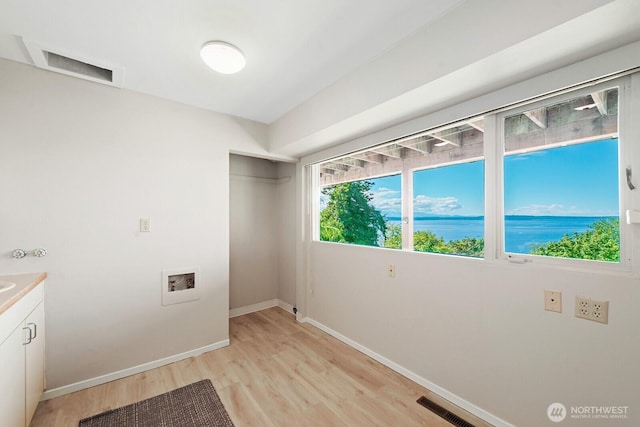 laundry room featuring cabinet space, light wood finished floors, washer hookup, baseboards, and a water view
