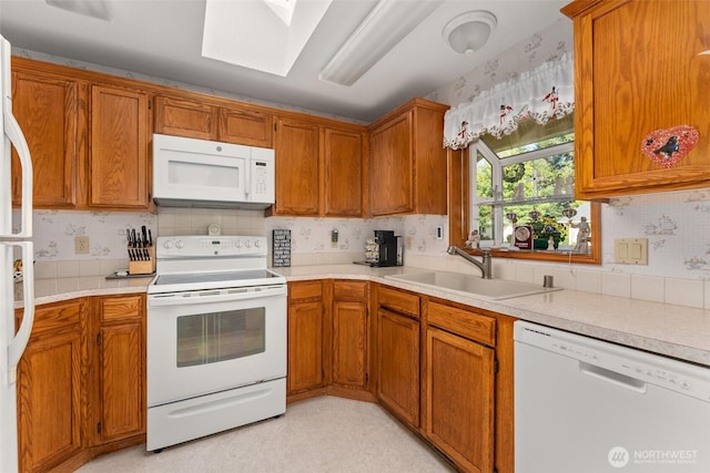 kitchen with white appliances, a skylight, a sink, and light countertops