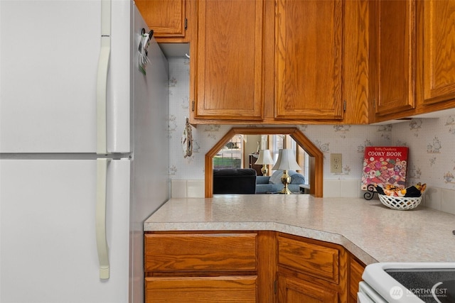 kitchen with freestanding refrigerator, brown cabinets, stove, and light countertops