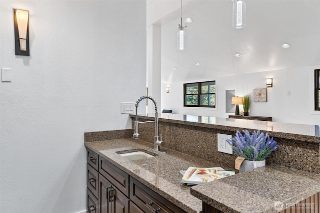 kitchen with a sink, a peninsula, decorative light fixtures, recessed lighting, and stone counters