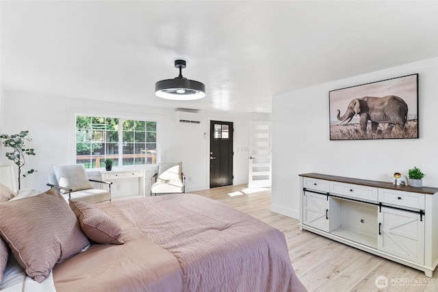bedroom featuring light wood-style floors, baseboards, and a wall mounted AC