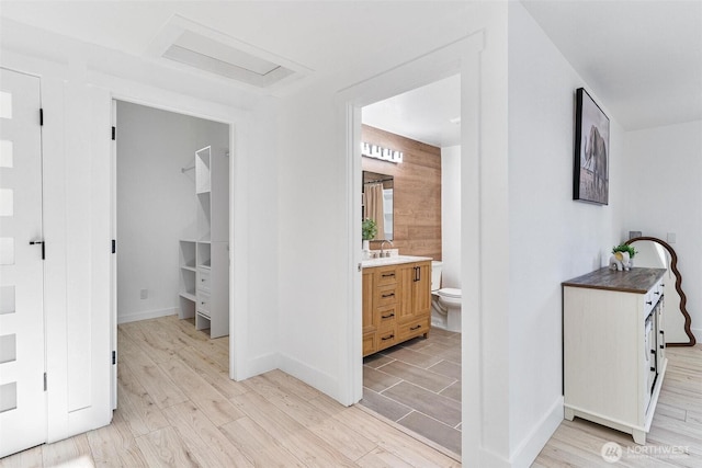 hall featuring light wood-style flooring, baseboards, and a sink