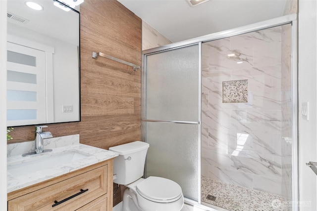 bathroom featuring toilet, a marble finish shower, wood walls, visible vents, and vanity