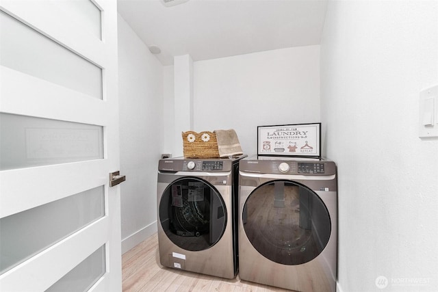 clothes washing area with light wood finished floors, laundry area, washer and clothes dryer, and baseboards