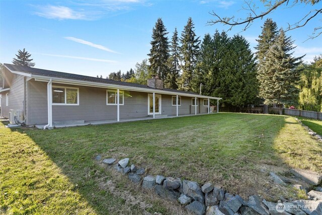 rear view of property with a chimney, a yard, and fence