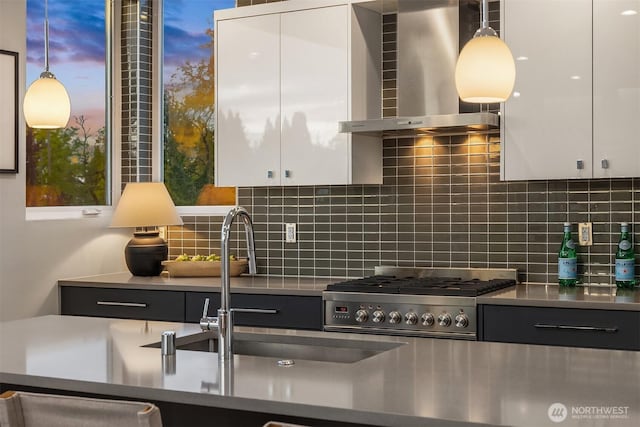 kitchen with wall chimney range hood, white cabinets, stainless steel counters, decorative backsplash, and gas range