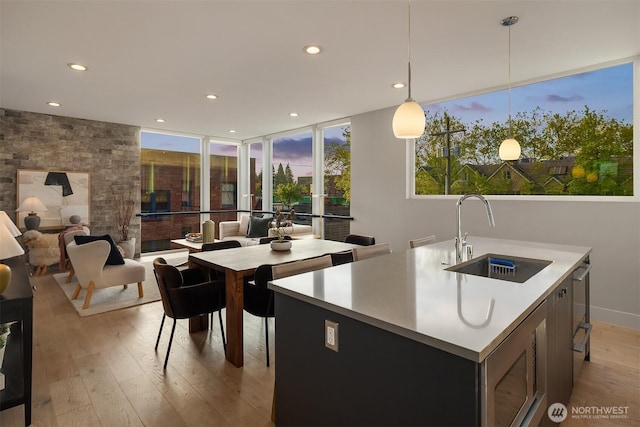 kitchen with pendant lighting, a center island with sink, light wood-type flooring, a sink, and recessed lighting