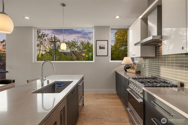 kitchen with a sink, wall chimney exhaust hood, stainless steel appliances, baseboards, and tasteful backsplash