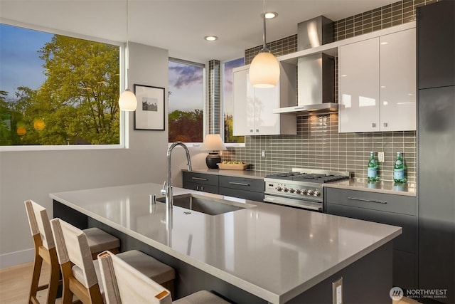 kitchen featuring a breakfast bar area, wall chimney exhaust hood, tasteful backsplash, high end stove, and a sink
