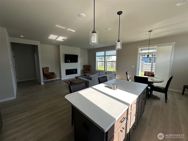kitchen featuring baseboards, dark wood-style floors, a center island, light countertops, and hanging light fixtures