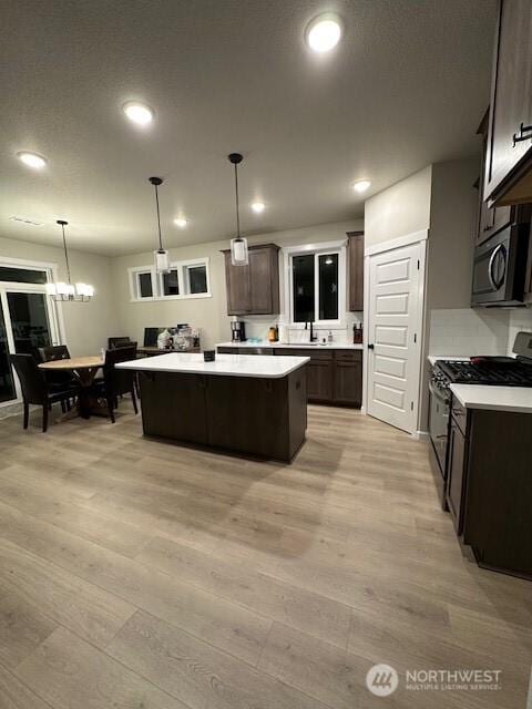 kitchen featuring dark brown cabinetry, a center island, light countertops, light wood finished floors, and stainless steel appliances