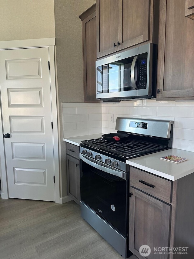 kitchen featuring light countertops, decorative backsplash, light wood finished floors, and stainless steel appliances