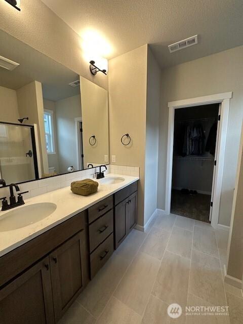 full bathroom featuring double vanity, visible vents, a shower stall, and a sink