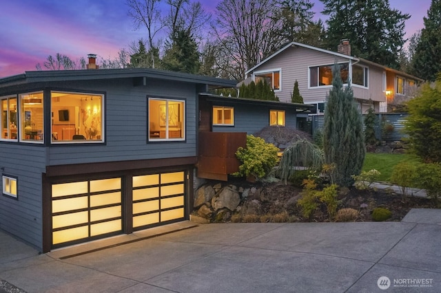 contemporary home with an attached garage, a chimney, and driveway