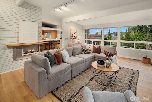 living area with brick wall, visible vents, track lighting, and light wood-style flooring
