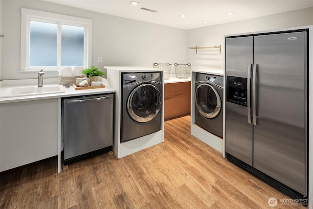 clothes washing area featuring visible vents, a sink, washer / dryer, and light wood finished floors