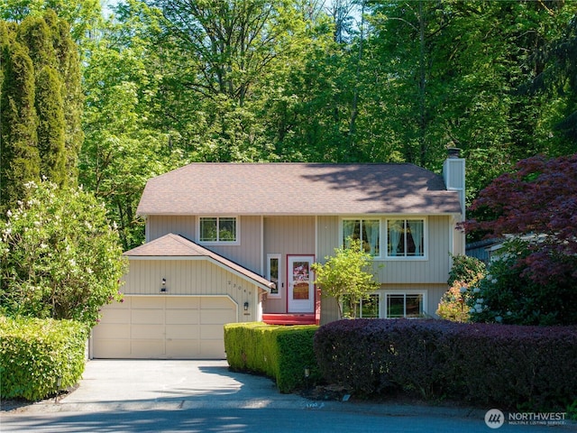 split foyer home featuring a garage, a chimney, driveway, and roof with shingles