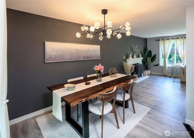 dining room featuring an inviting chandelier, a fireplace with raised hearth, baseboards, and wood finished floors