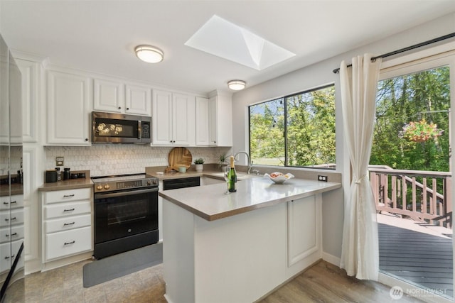 kitchen with stainless steel appliances, white cabinetry, a peninsula, tasteful backsplash, and a skylight