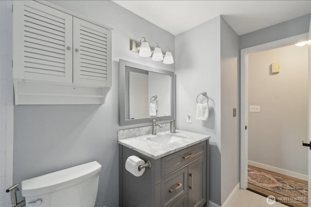 half bath with toilet, baseboards, and vanity