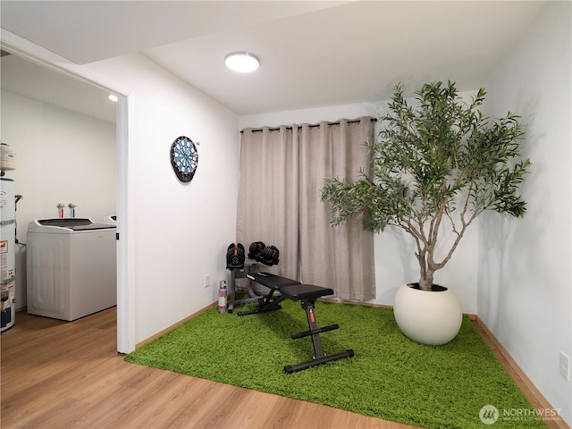 exercise room featuring washer / dryer, baseboards, secured water heater, and wood finished floors