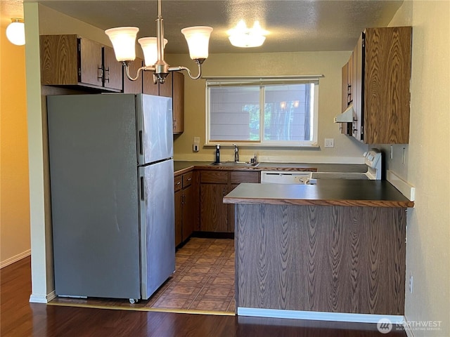 kitchen featuring freestanding refrigerator, a peninsula, under cabinet range hood, a sink, and range