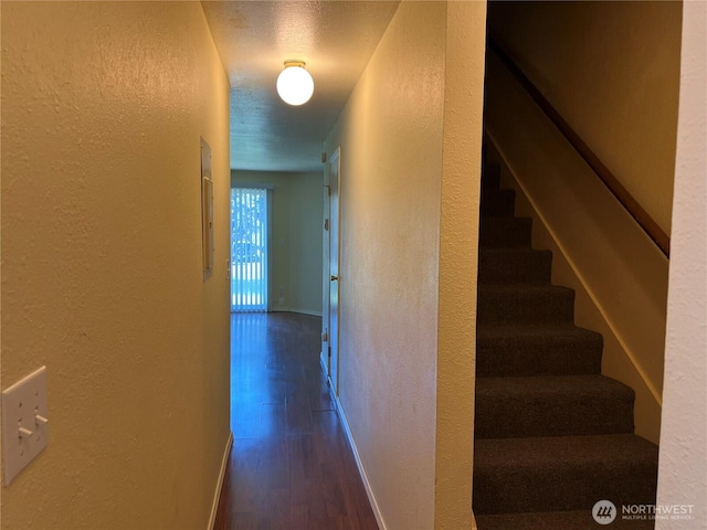 corridor with baseboards, a textured wall, dark wood-style floors, and stairs