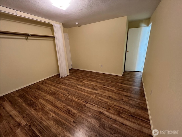 unfurnished bedroom featuring dark wood-style flooring, baseboards, a textured ceiling, and a closet