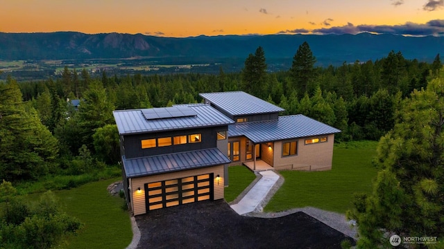 view of front of home featuring a standing seam roof, roof mounted solar panels, metal roof, a view of trees, and a yard