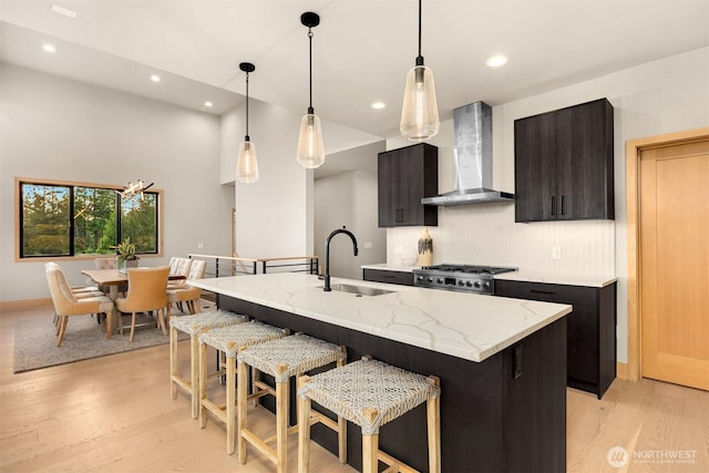 kitchen with wall chimney range hood, tasteful backsplash, a sink, light wood-type flooring, and a kitchen bar
